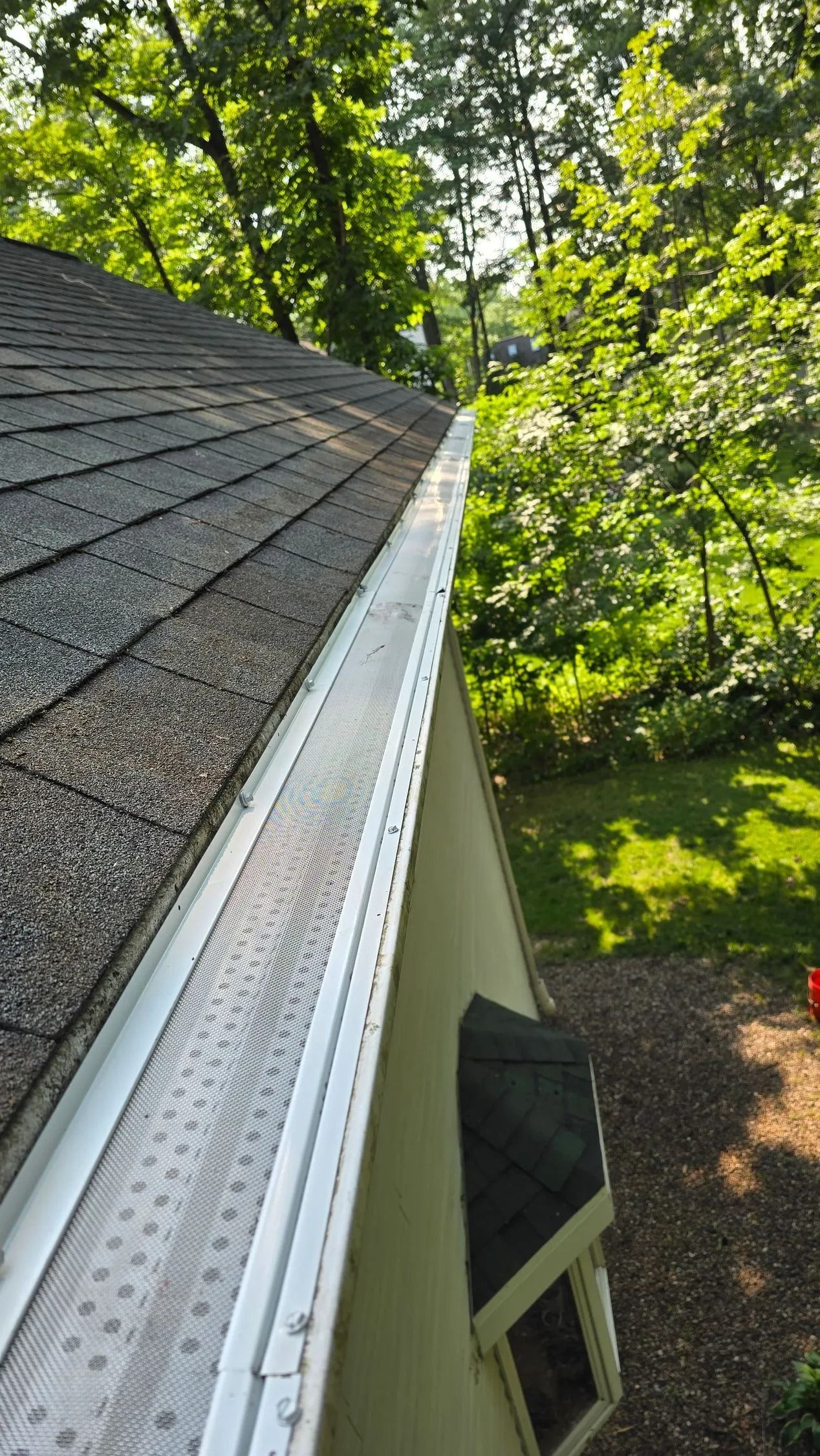 House roof edge with white gutter beside green trees and yard