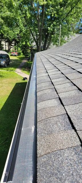 Roof shingles and gutter along a sloped roof beside a grassy yard and trees