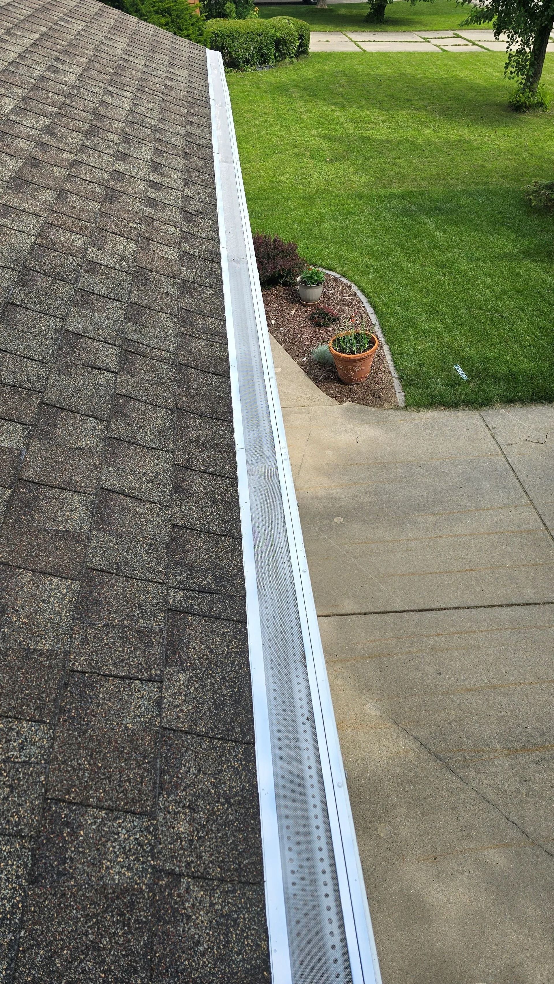 Roof edge with white gutter beside a concrete walkway and green lawn.