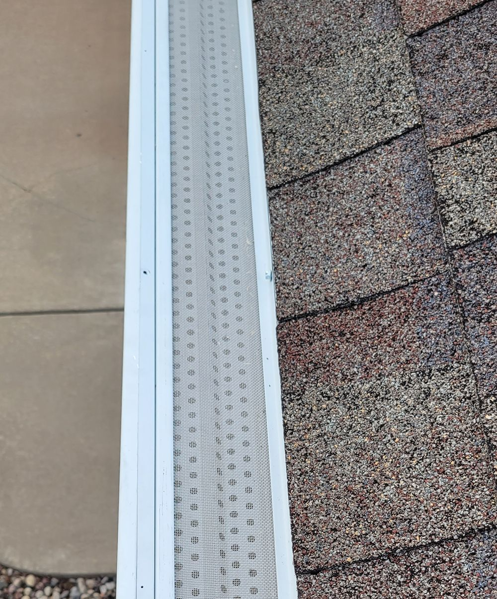 White gutter beside roof shingles and a beige wall panel, showing a close-up of a building edge.