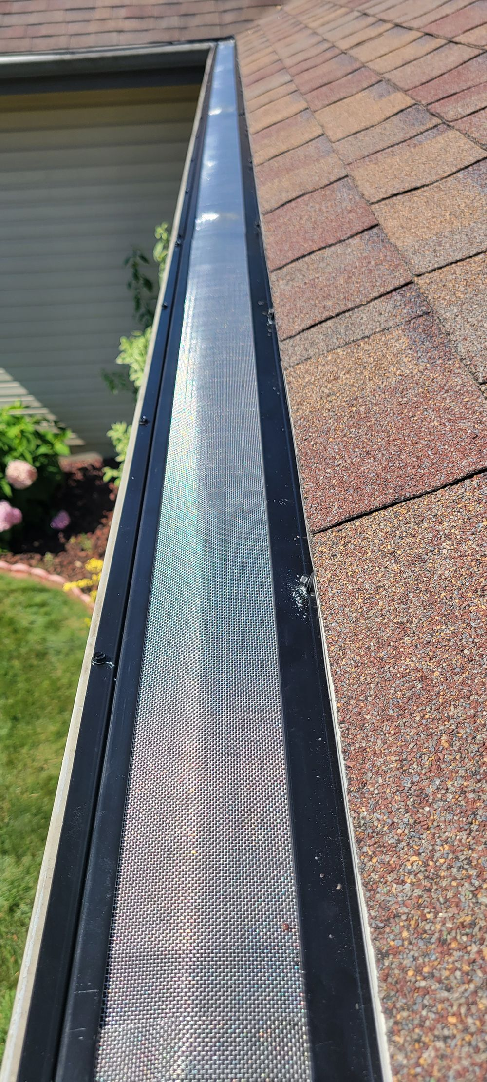 Gutter along a shingled roof with water flowing through, viewed from above.