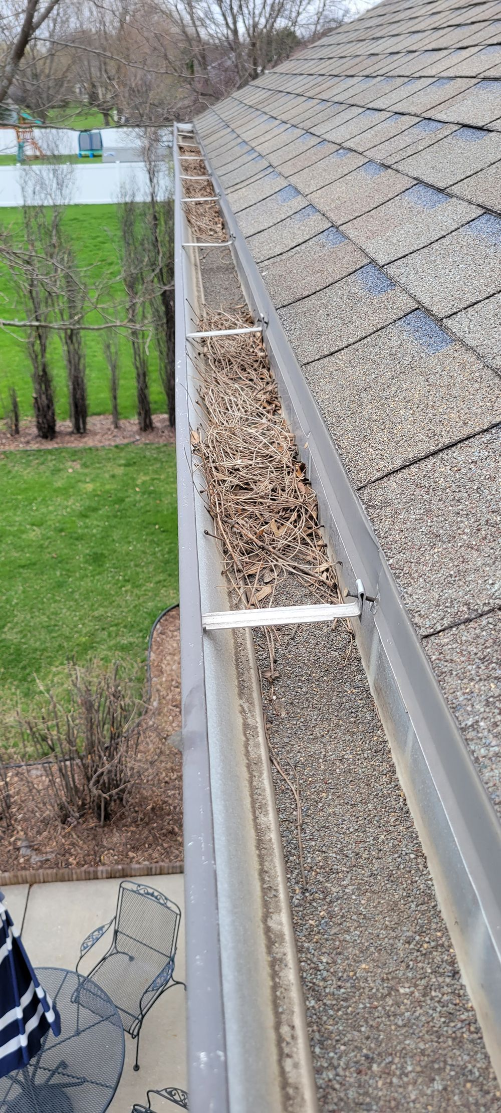 View from a rooftop walkway with metal railing beside a steep shingled roof and trees below