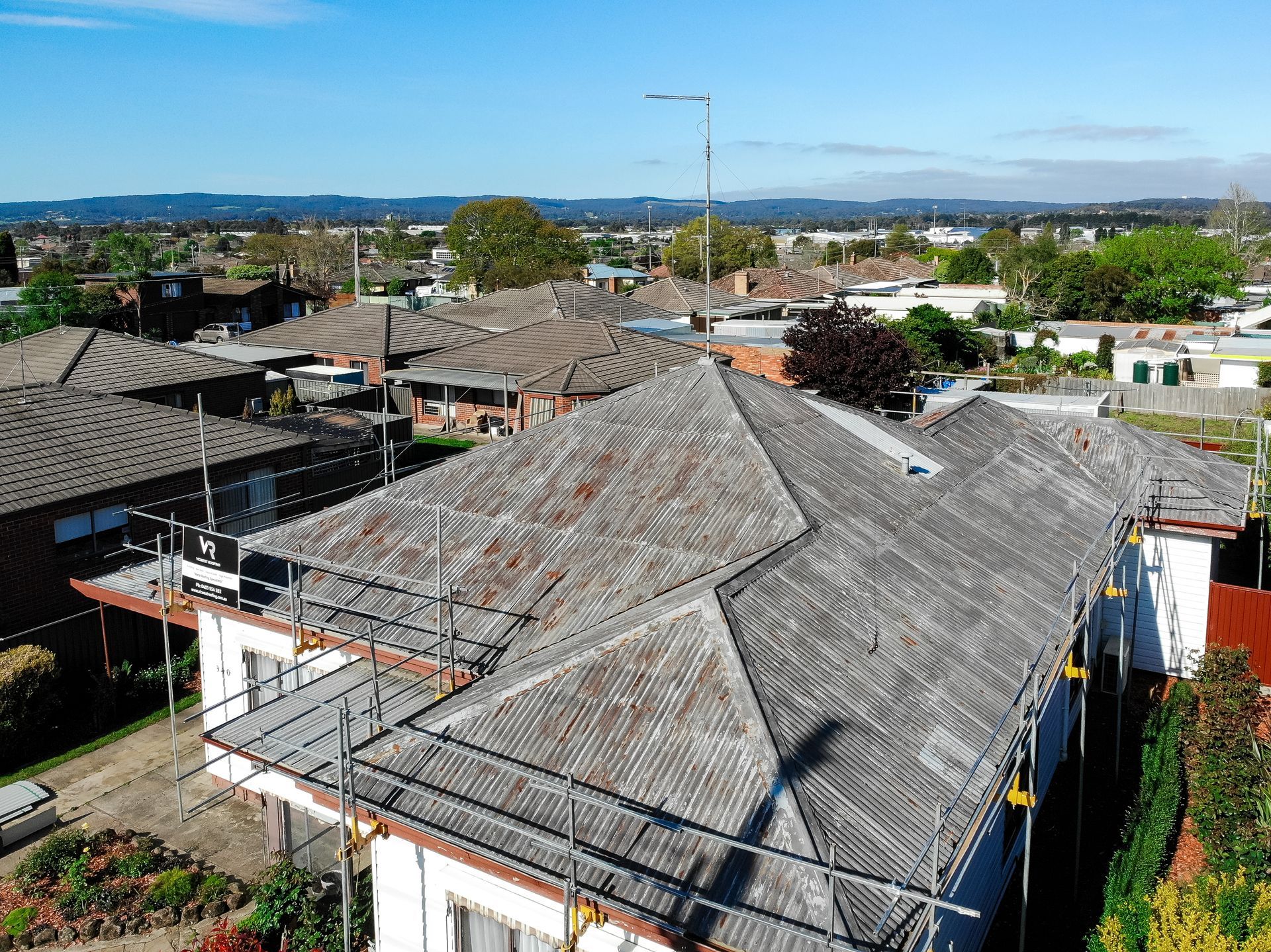 Before, rusted corrugated metal roof on a long single-storey weatherboard home with scaffolding, Wendouree VIC.