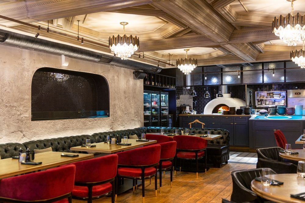 Upscale restaurant interior with dark red chairs, tufted black booths, wooden tables, and elegant chandeliers.