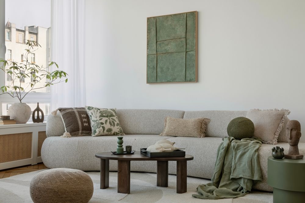A cozy living room with a curved, light-colored sofa, earth-toned pillows, a wooden coffee table, and green decor accents.
