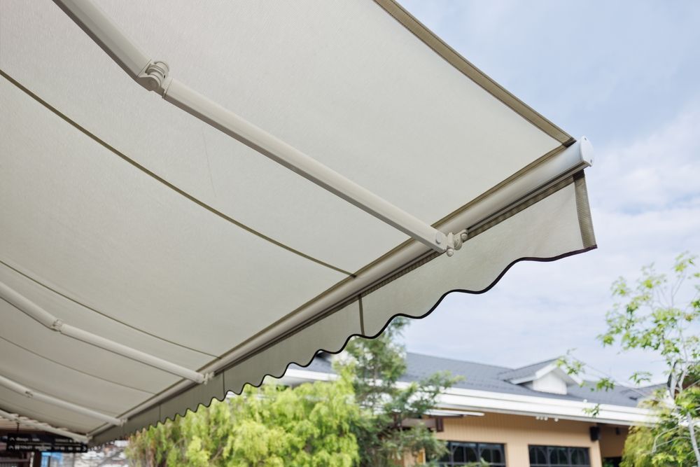 A retractable off-white fabric awning extended outward over a view of trees and a house roof.