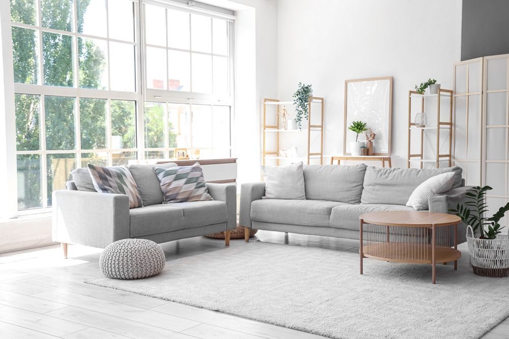 A light-filled living room featuring two gray sofas, a wooden coffee table, a white rug, and decorative shelves.