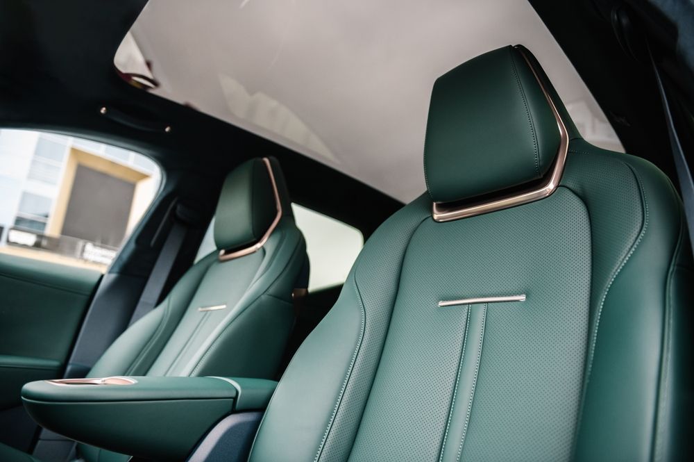 Green leather car seats with copper-colored trim and a panoramic glass roof in the interior of a vehicle.
