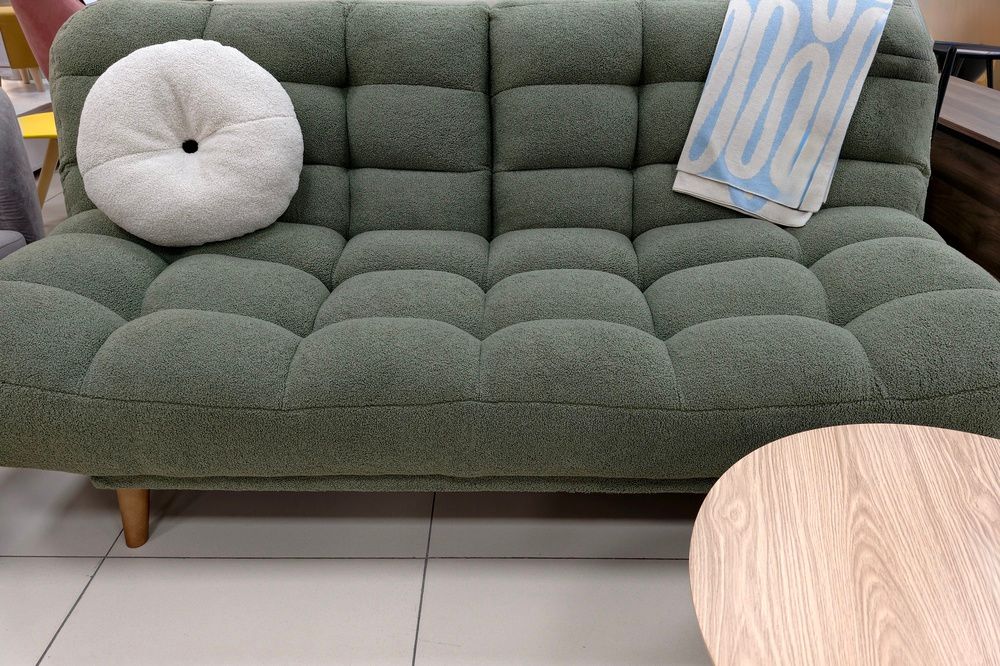 A green tufted sofa with a white round pillow and a blue and white patterned throw blanket in a room.