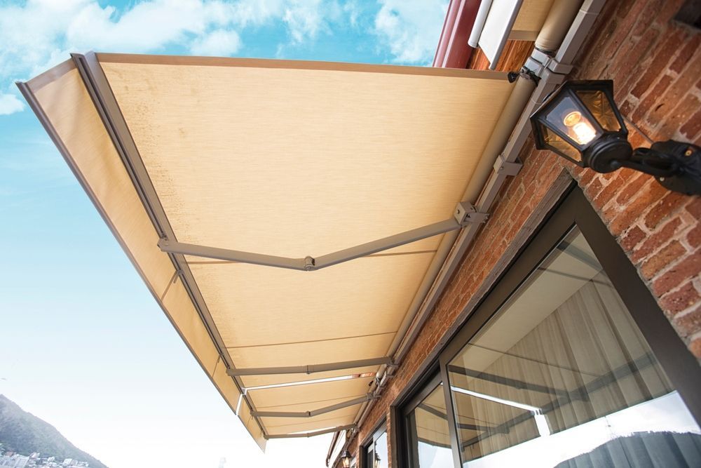 A beige retractable awning extended outward from a brick building exterior, positioned above a glass sliding door.