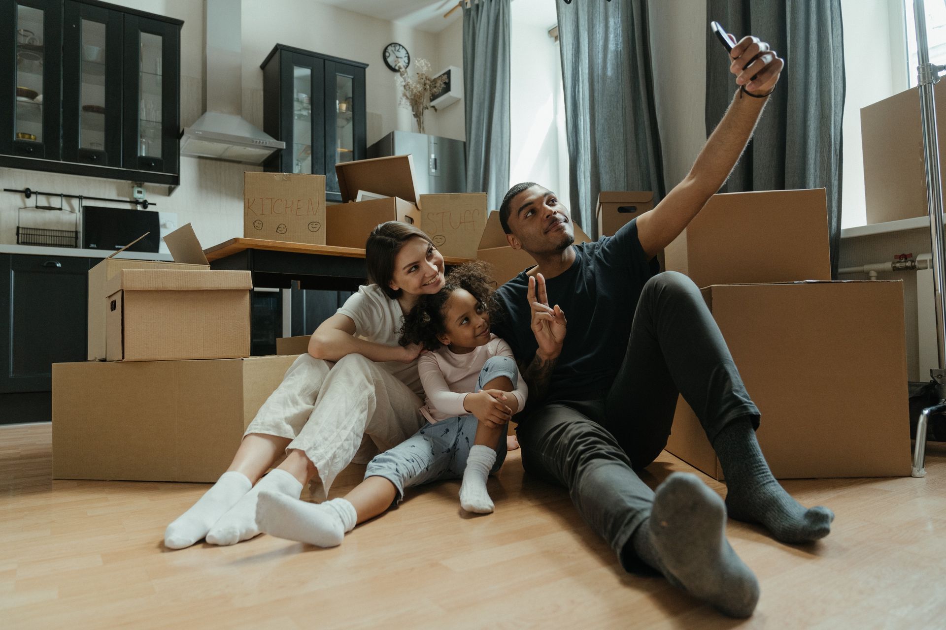 A family is sitting on the floor taking a selfie in their new home.