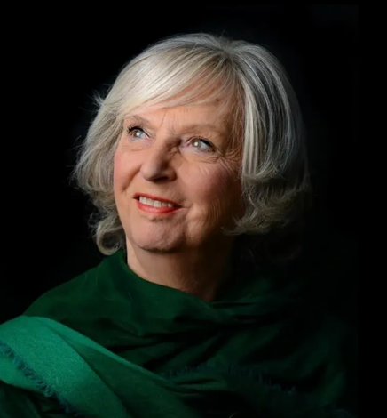 Portrait of a smiling woman with short white hair in a green shawl against a dark background