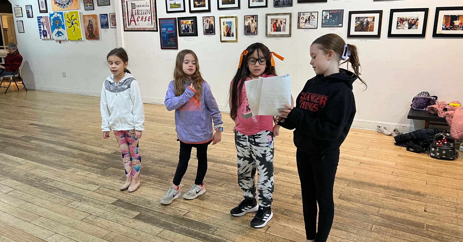 Four children stand and pose in an art gallery with framed artworks on the walls.