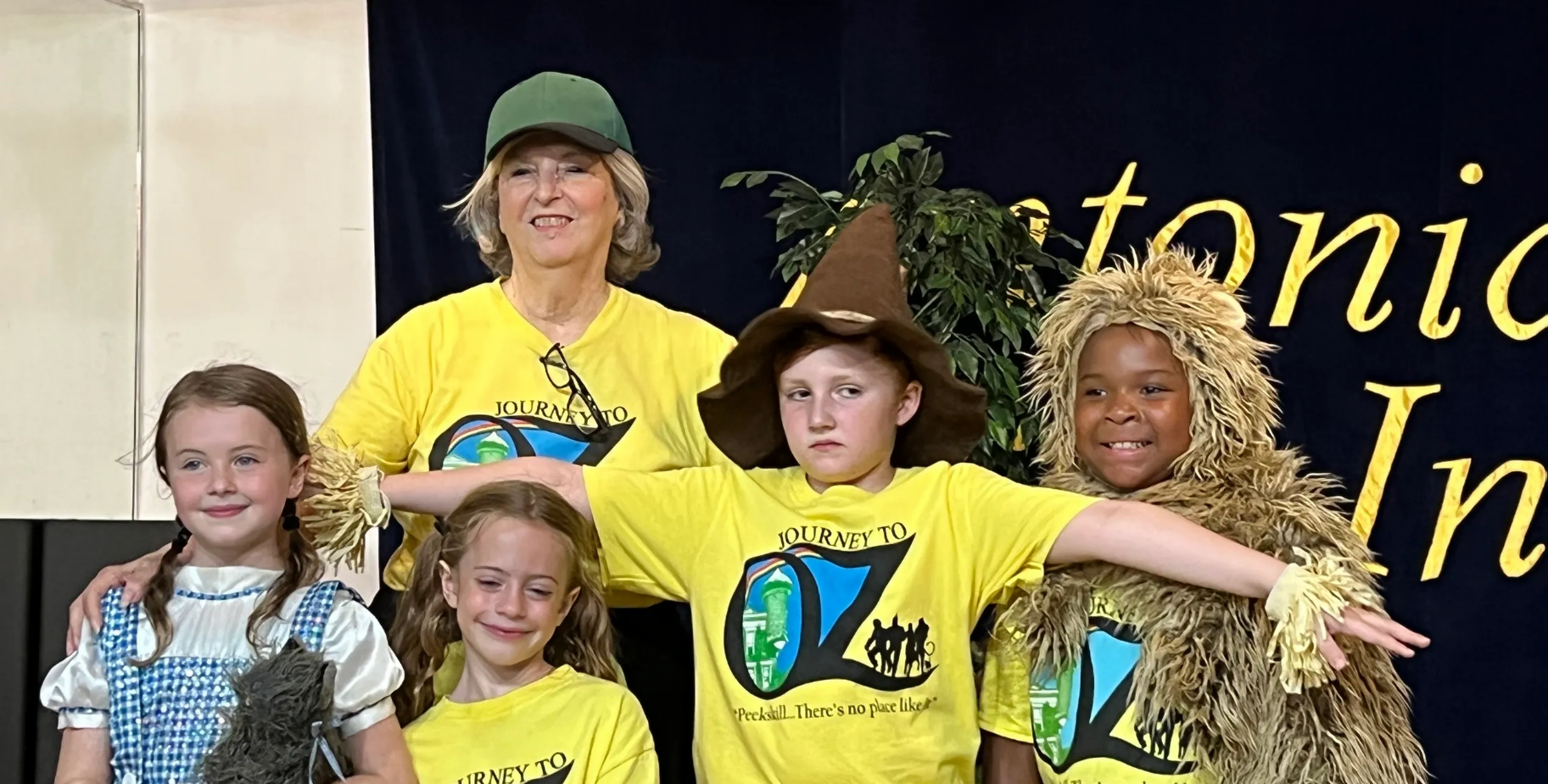 Four children in yellow shirts posing in costumes on a stage backdrop.