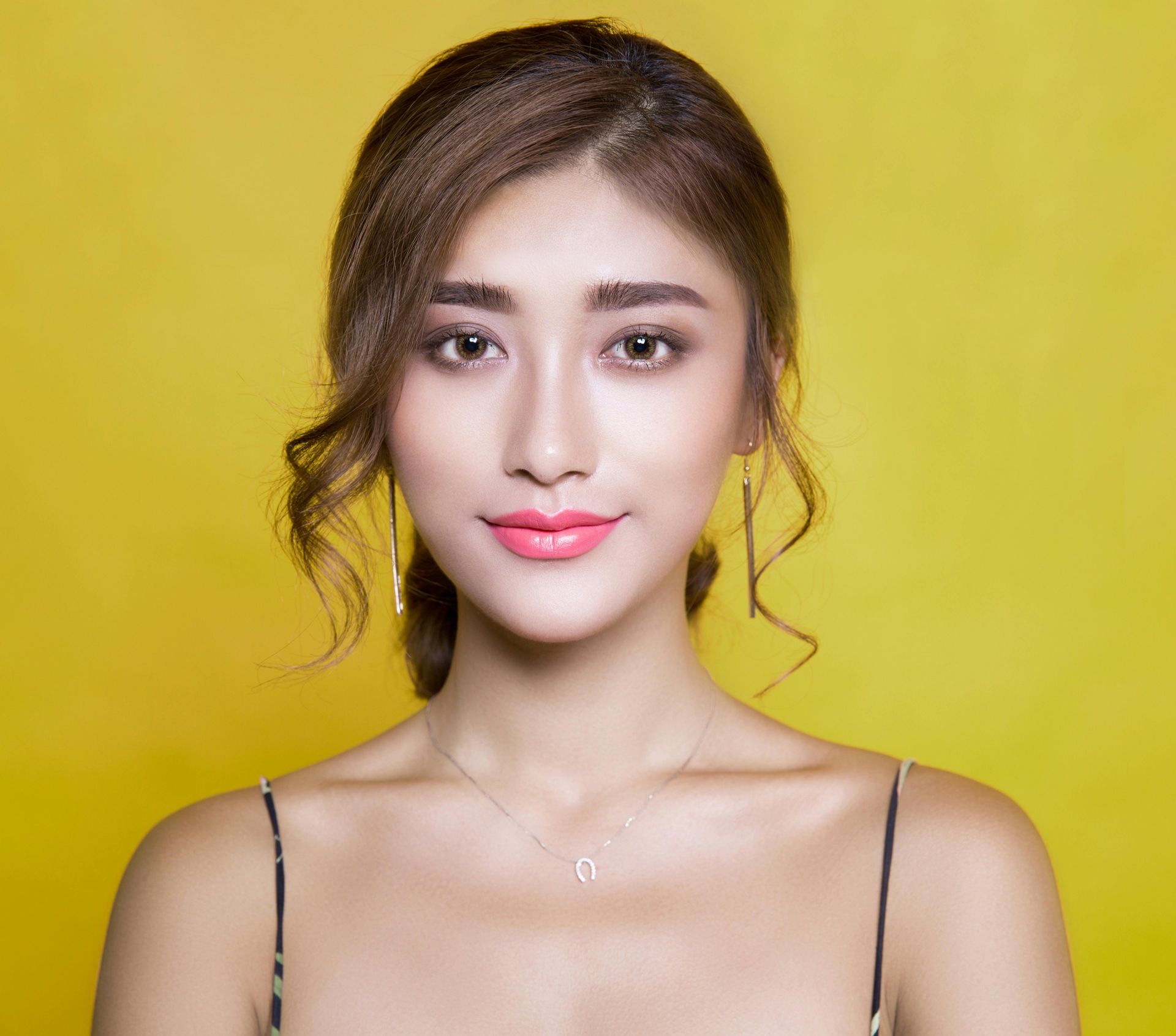 Young woman with brown hair and makeup, against a yellow background.