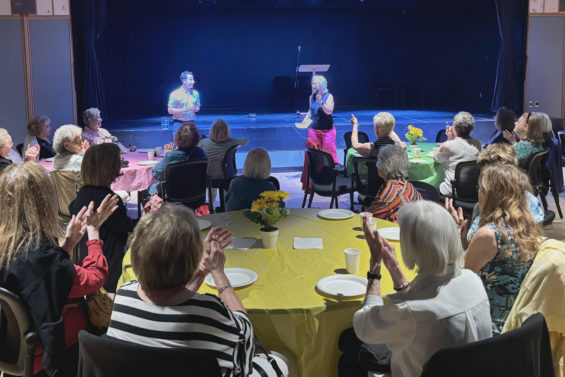 Un groupe de personnes sont assises à des tables devant une scène