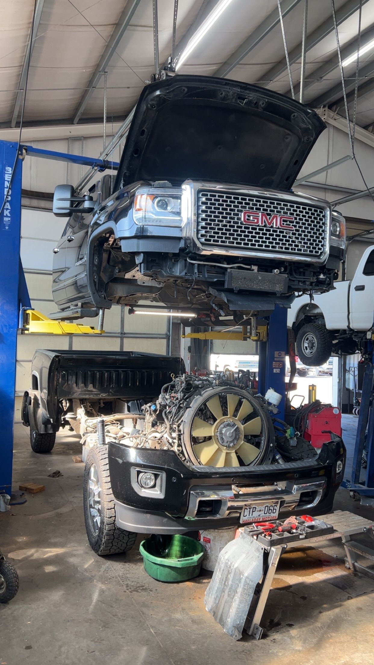 Two vehicles stacked in an auto shop, top car on a lift over a black SUV with its hood open.