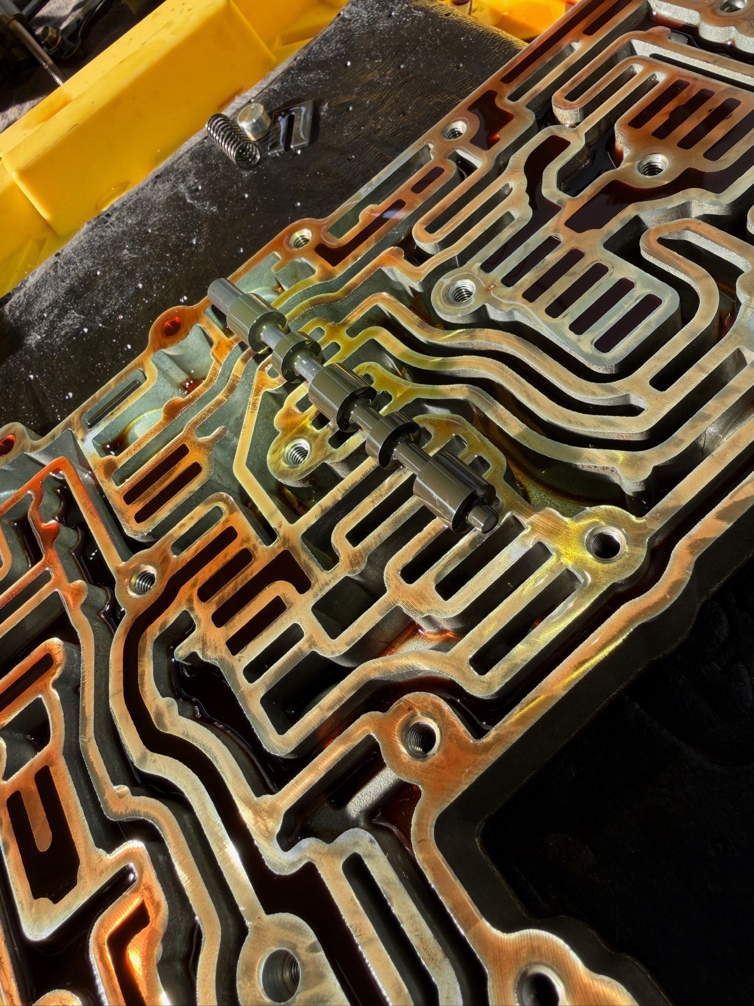 Close-up of a dirty metal gasket or engine part with intricate channels, resting on a yellow surface.