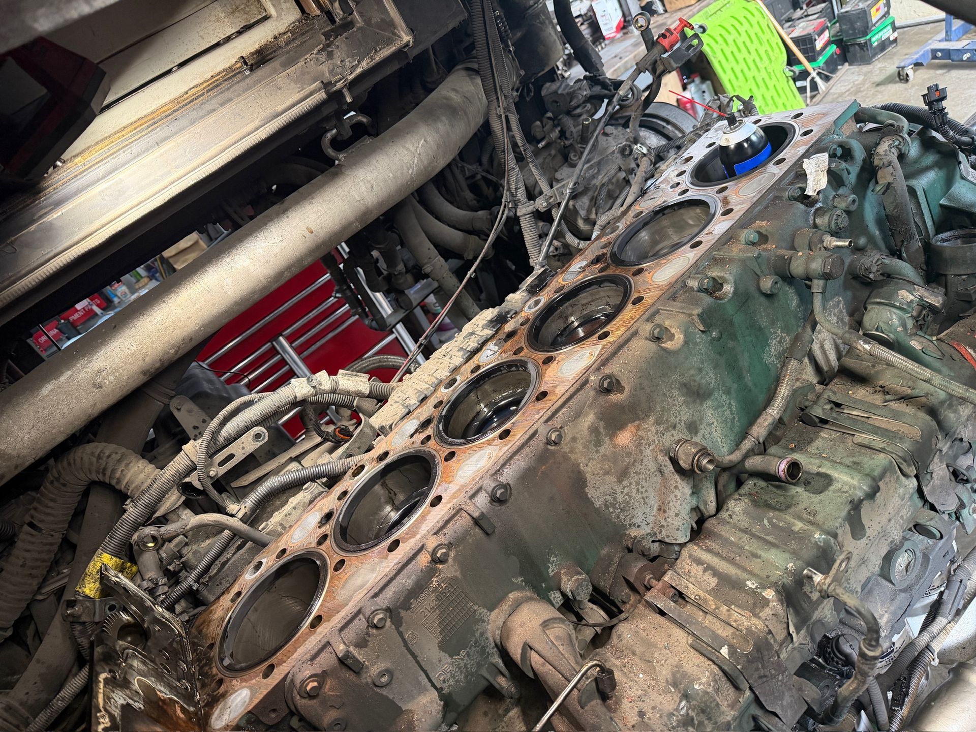 Damaged truck engine block and parts under a raised vehicle in a repair shop