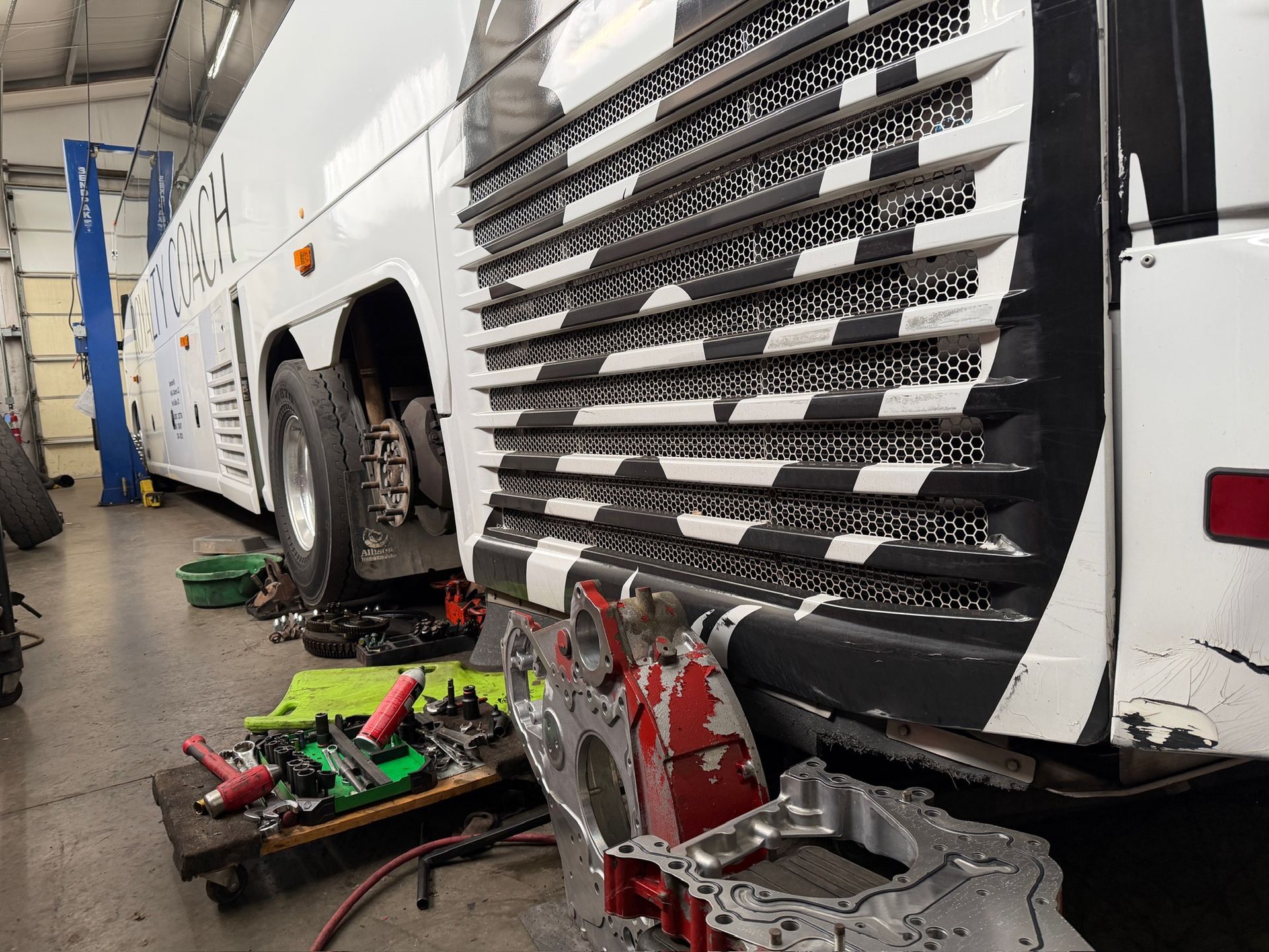 White vehicle in a repair shop with a damaged side panel and tools scattered on the floor.