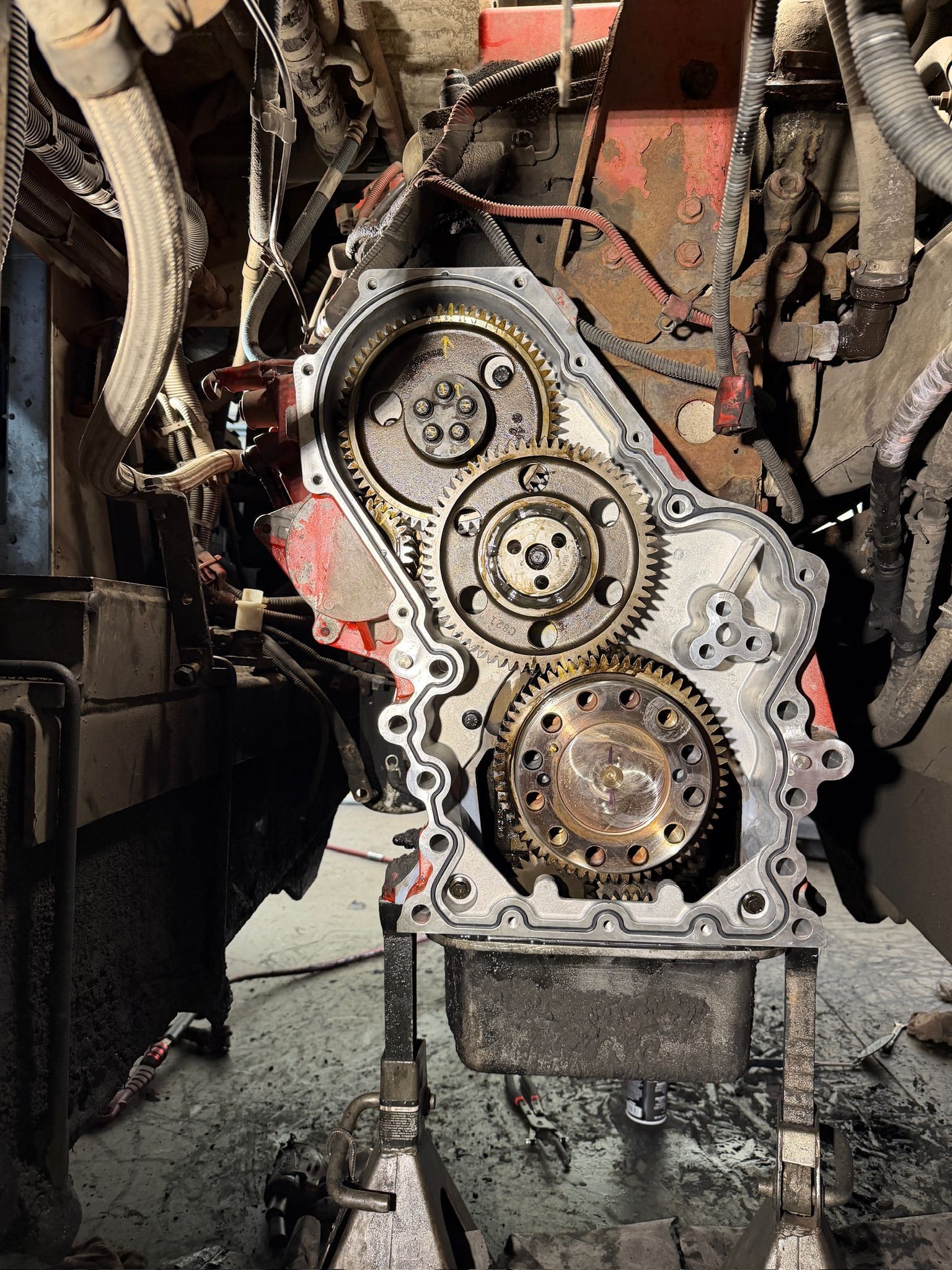 Exposed engine block with timing gears and gasket, coated in oil and grime inside a workshop.