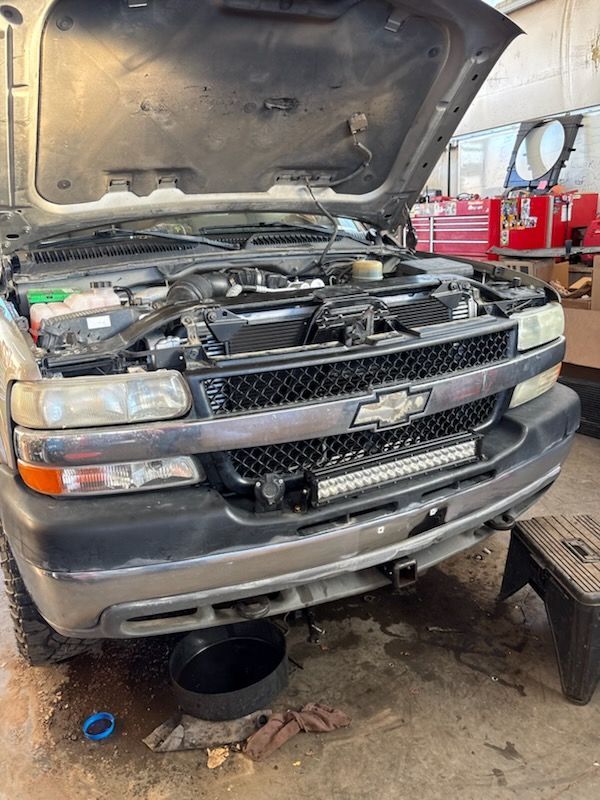 Gray Chevy truck with hood open in a garage, showing the engine compartment and front bumper.