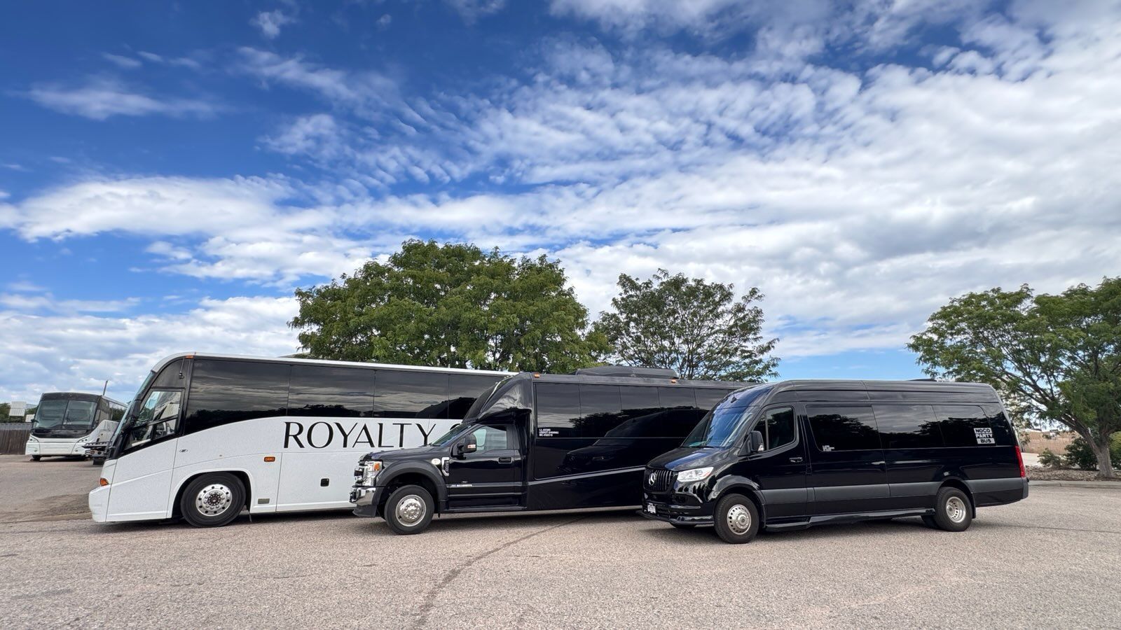Black SUV, black van, and white coach bus in a parking lot under a cloudy sky
