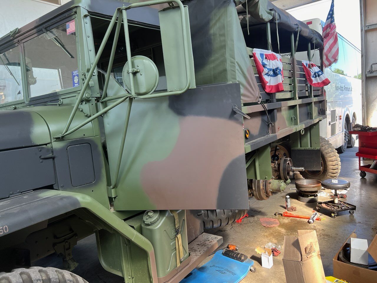 Military truck under repair in a workshop, with tools and parts scattered nearby.