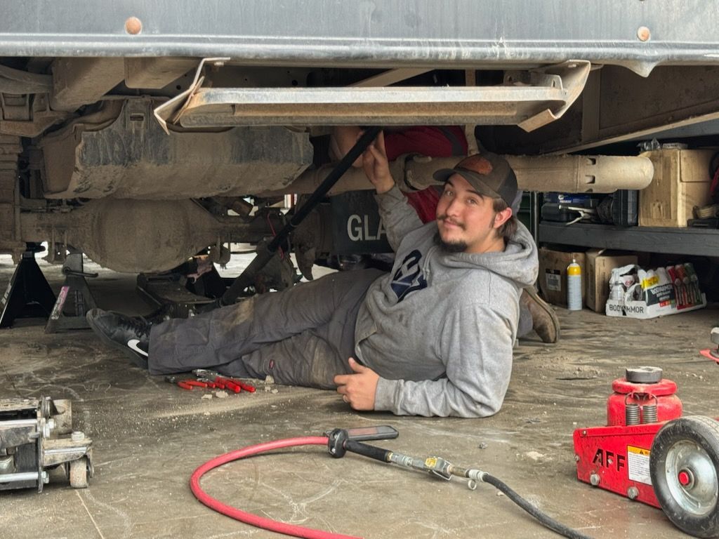 Mechanic lying under a vehicle on concrete floor, holding a tool in a garage with red equipment nearby