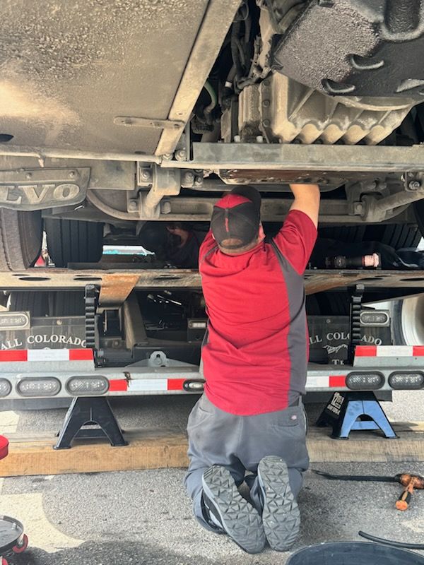 Person kneeling under a vehicle, working on the undercarriage in a garage.