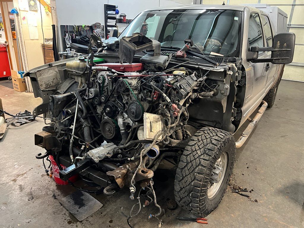 Damaged black pickup truck with front end removed, parked in a garage workshop