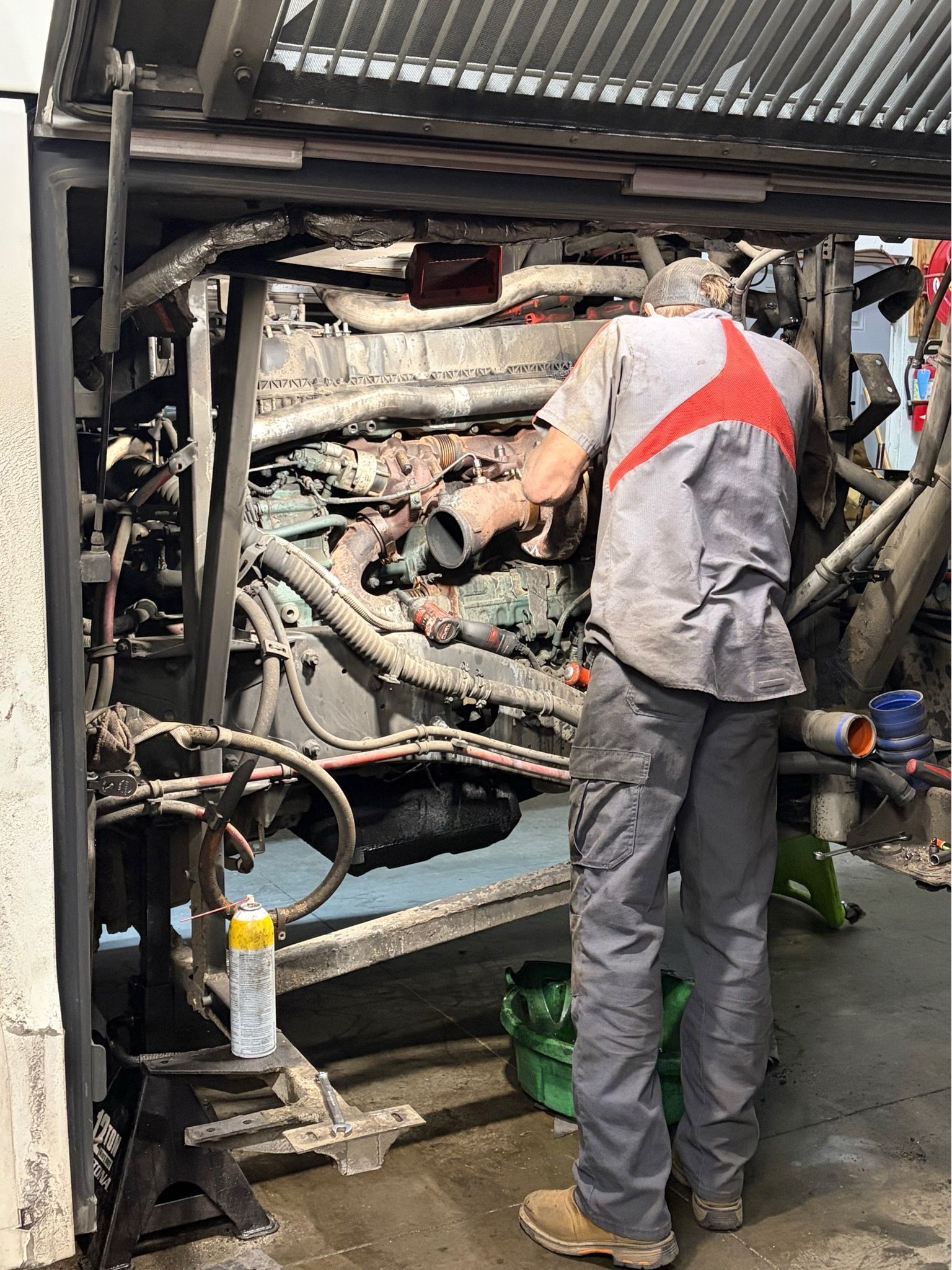 Technician inspecting machinery inside an industrial compartment, wearing gray coveralls with orange safety stripes.