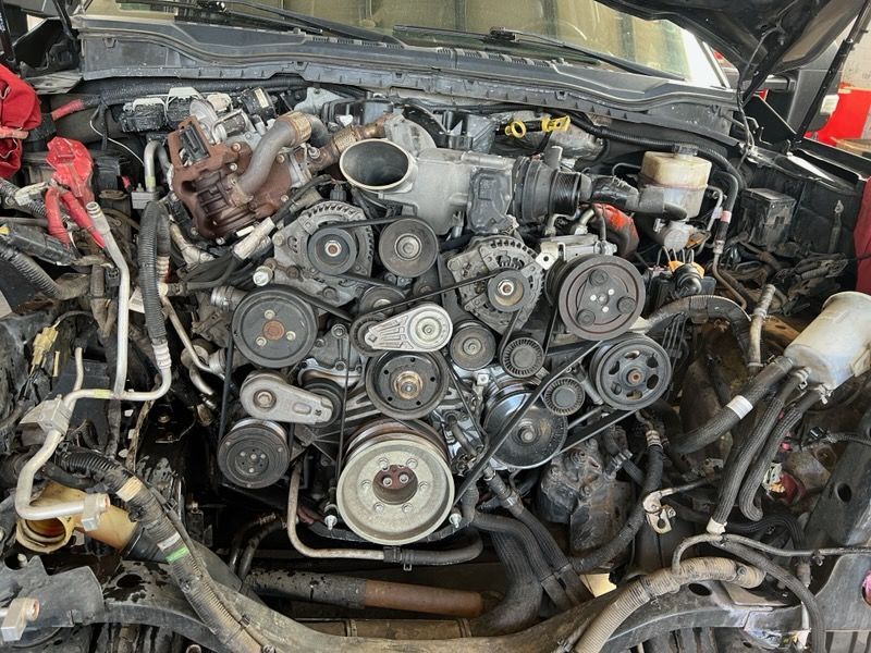 Car engine bay with exposed serpentine belts and pulleys, showing extensive mechanical components.