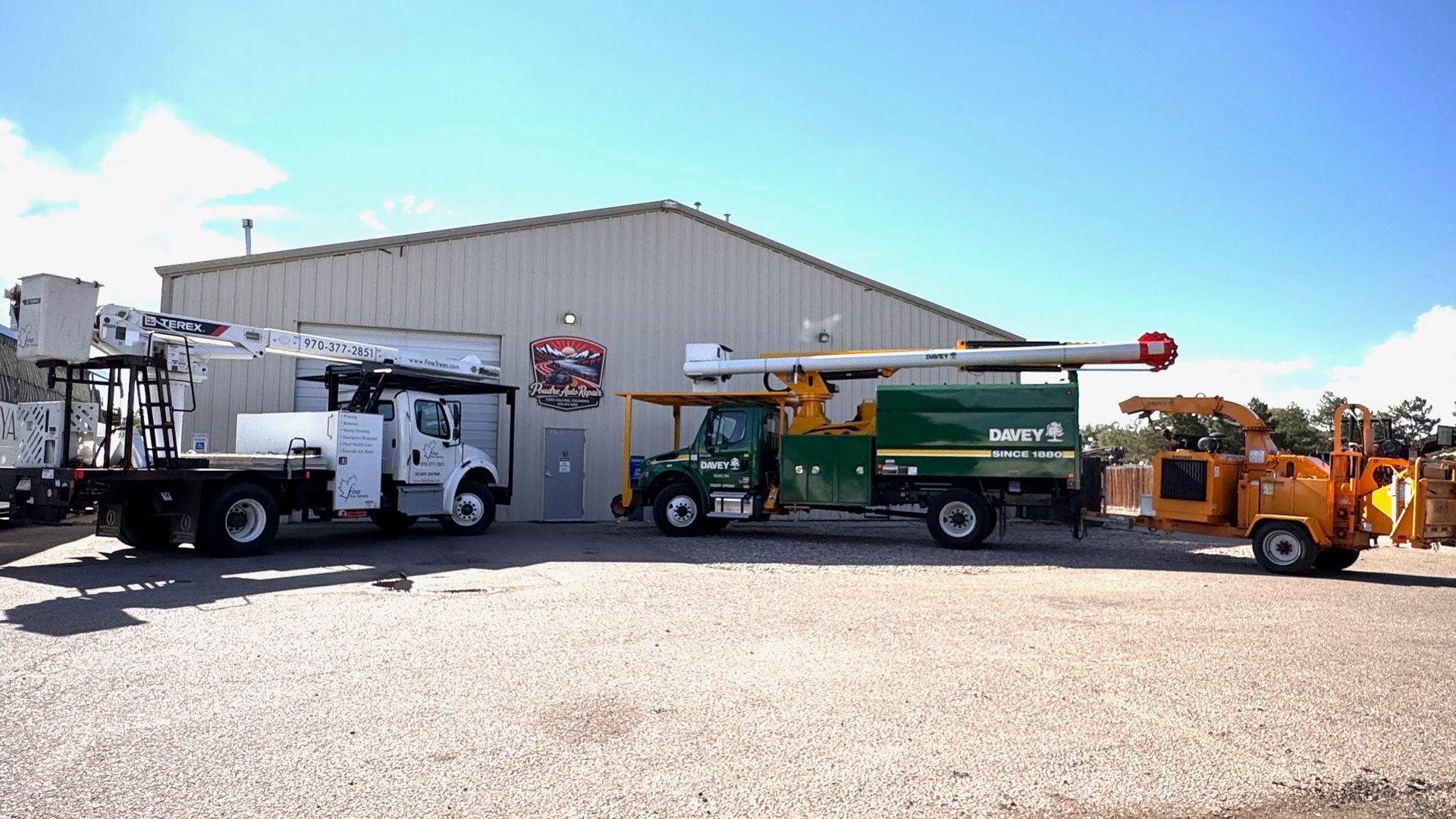 Line of utility trucks and a crane parked in front of a large metal warehouse.