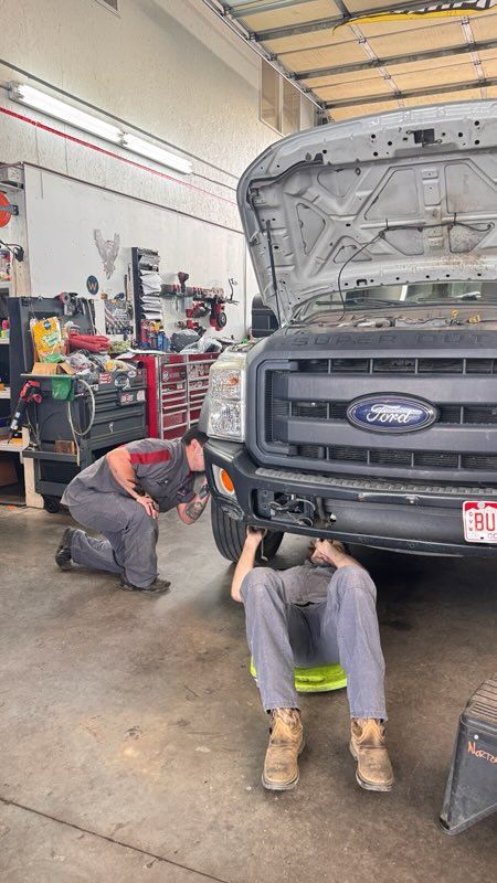 Mechanics working under the front of a lifted truck in an auto repair shop