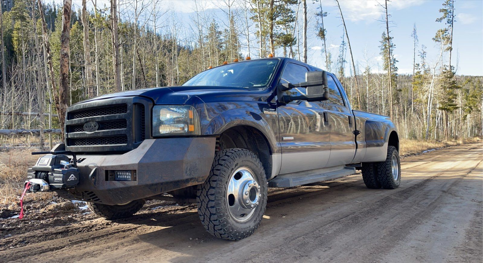 Black pickup truck parked on a muddy dirt road in a wooded area under a clear sky