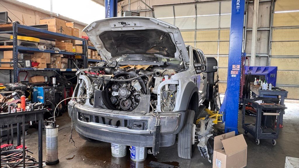 Damaged silver SUV in an auto repair shop with hood open and front end disassembled