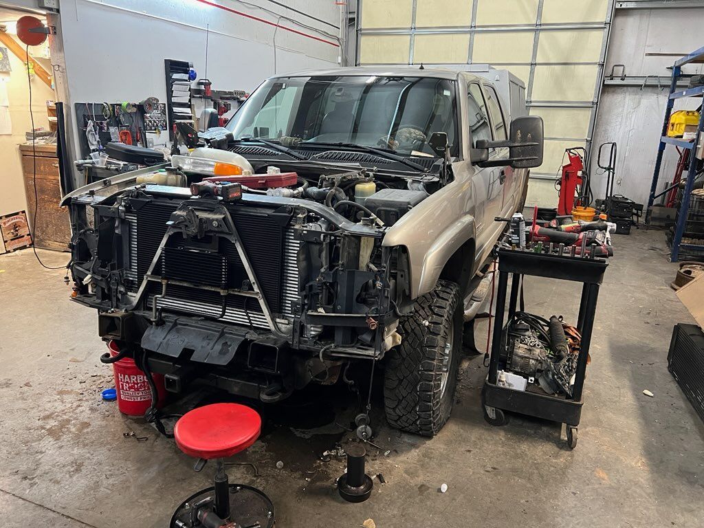 Pickup truck undergoing repairs in an auto shop, front end removed and tools nearby.