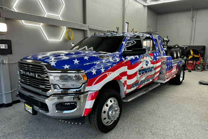 American flag-themed tow truck parked inside a garage. The truck is white, red, and blue with “Towing” branding.