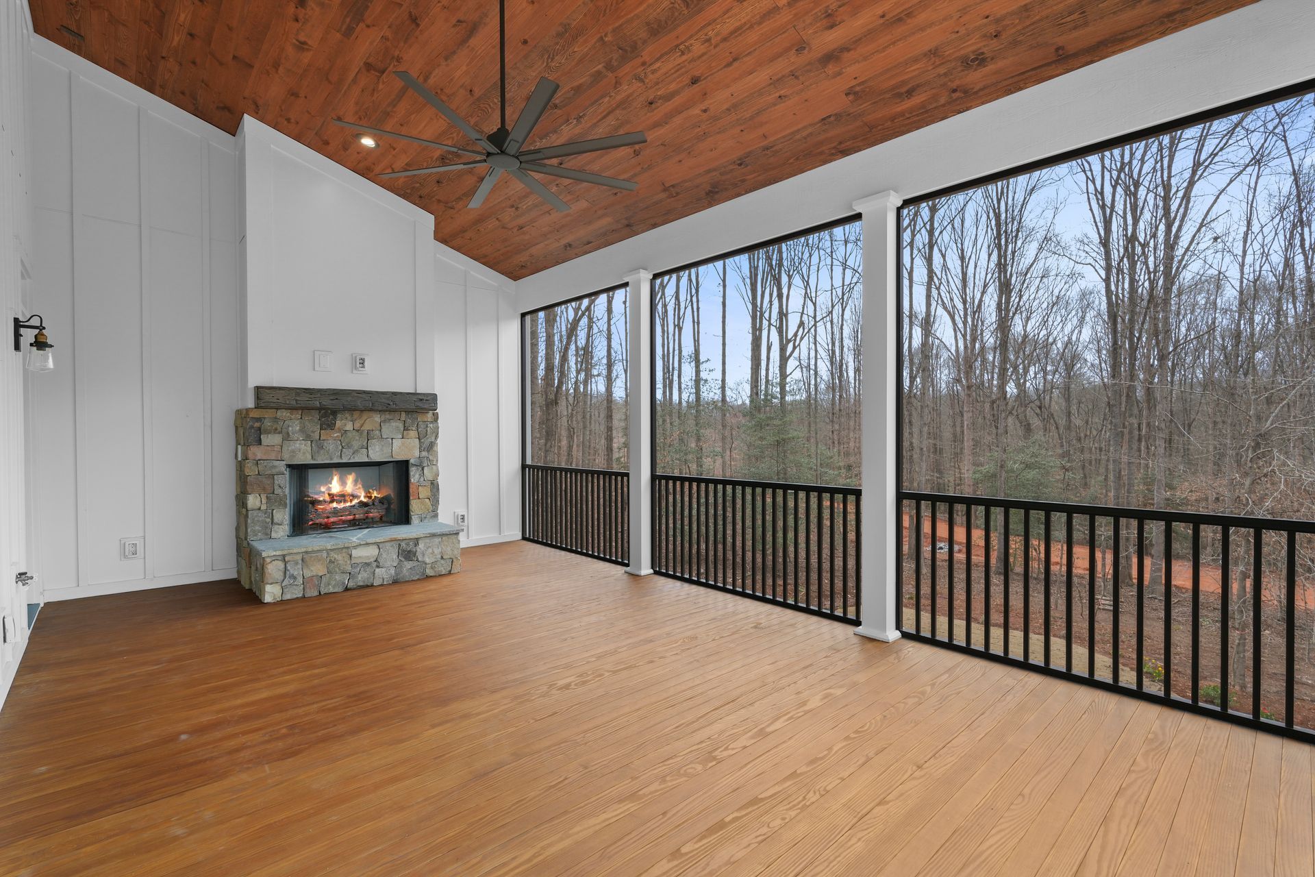 A screened in porch with a fireplace and a ceiling fan.