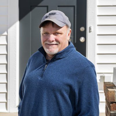 A man wearing a hat and a blue sweater is standing in front of a door.