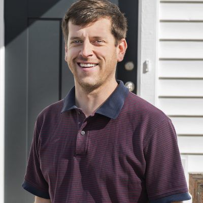 A man in a purple polo shirt is smiling in front of a door.