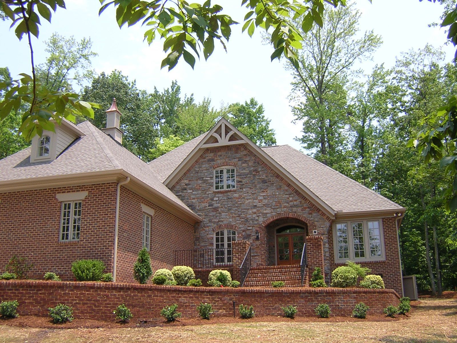 A large brick house with a brown roof is surrounded by trees