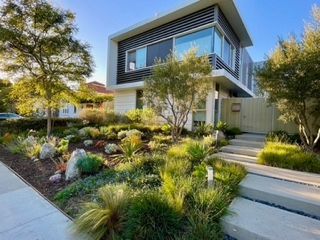 Modern two-story house with landscaped front yard, gray steps leading up. Sunny day.
