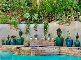 Backyard pool with succulents and cacti in turquoise pots along a stone wall with a waterfall feature.
