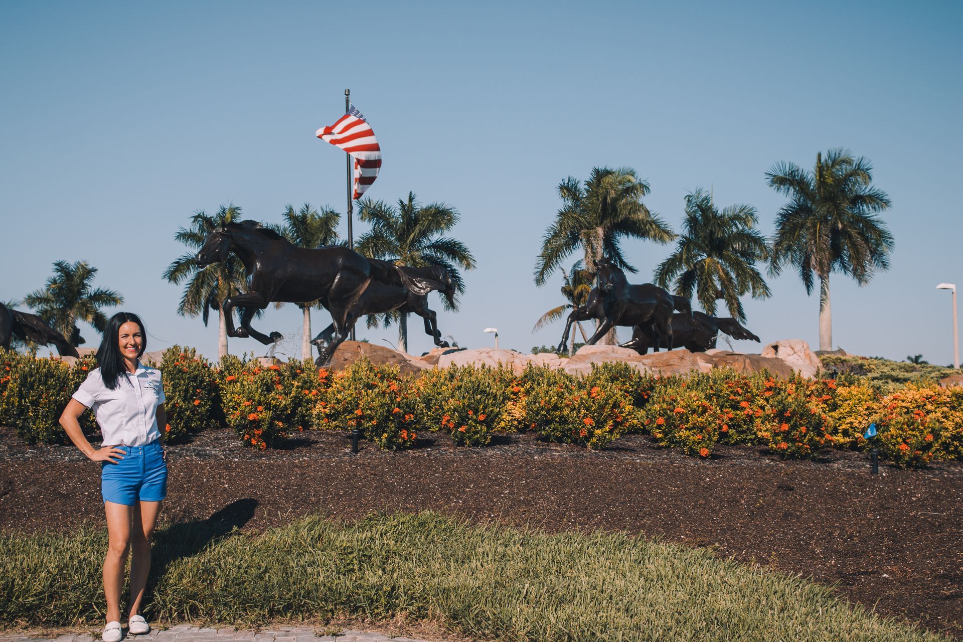 A woman is standing in front of a statue of a horse and a flag.