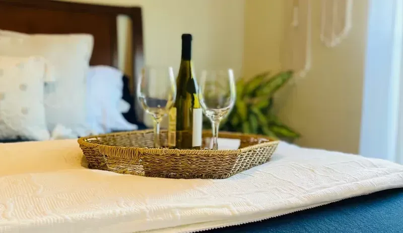 A tray with a bottle of wine and two glasses on a bed.