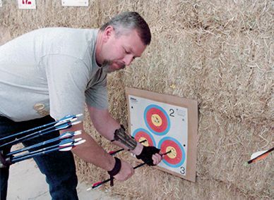Man removing arrows from a target at an archery range. He wears a wrist guard and finger tab.