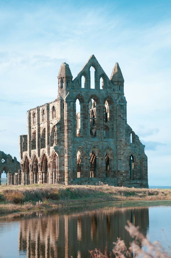The ruins of Whitby Abbey reflected in still water under a blue sky
