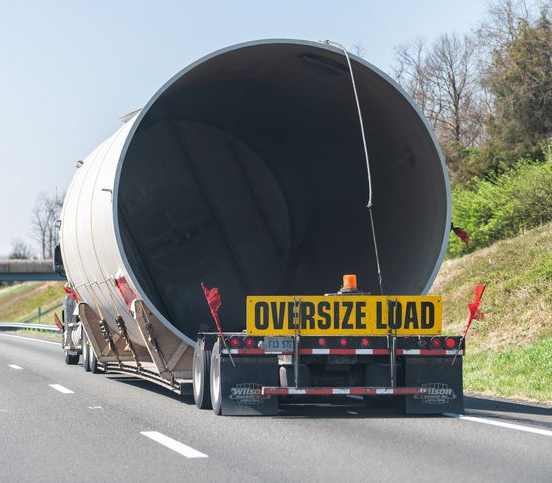 A large cylindrical object is transported on a trailer truck, with 